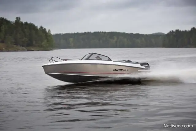 A Falcon 18 R speedboat glides across a calm lake, surrounded by lush green trees under a cloudy sky.
